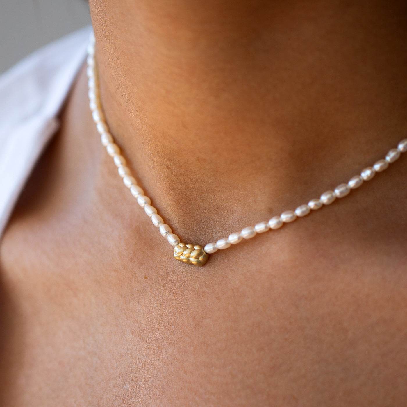 closeup of a women wearing challah pendant in 14k yellow gold,  with pearls chain