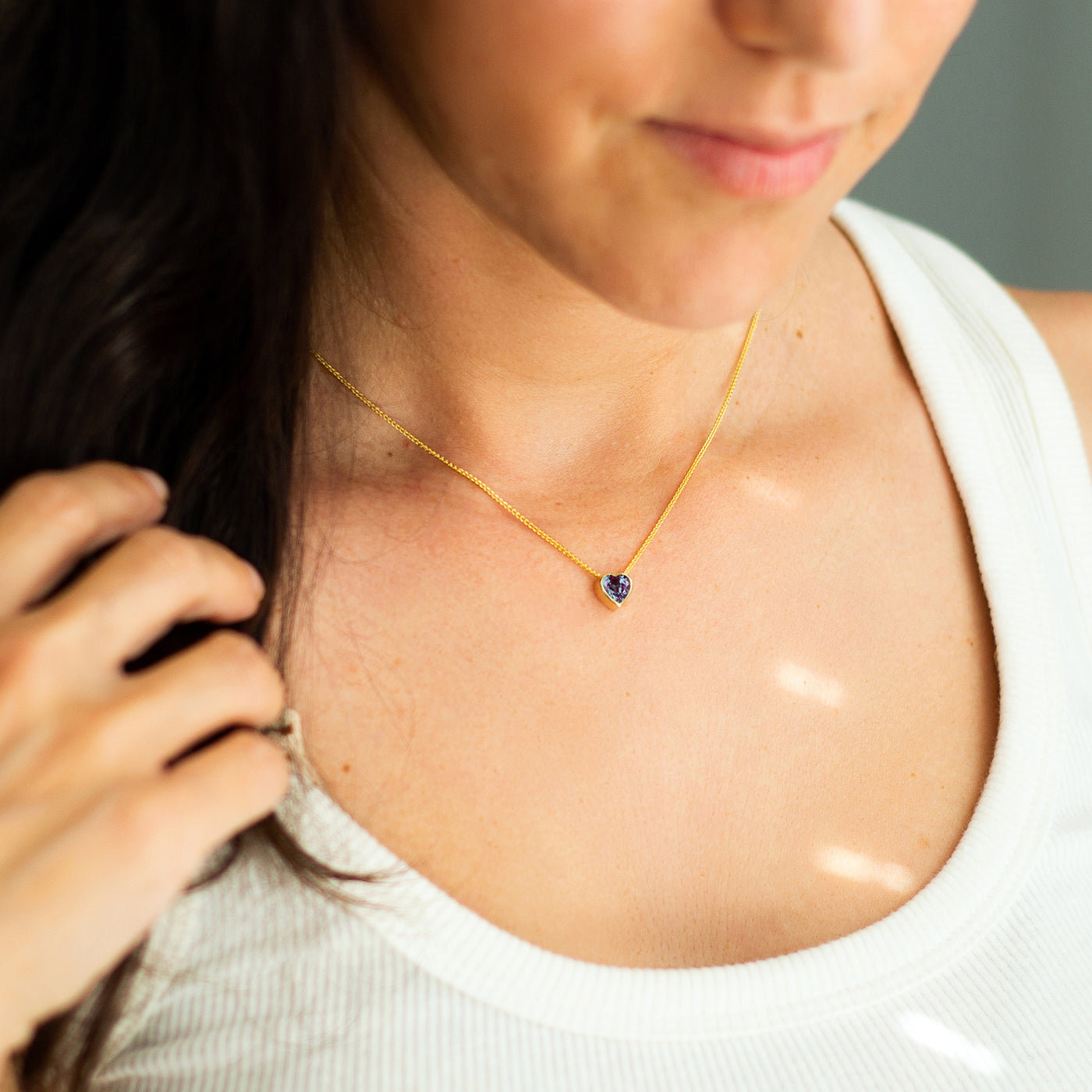 Woman wearing a gold Alexandrite necklace on a neutral background