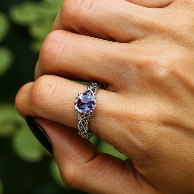Hand wearing a ring with a purple gemstone against a blurred green background