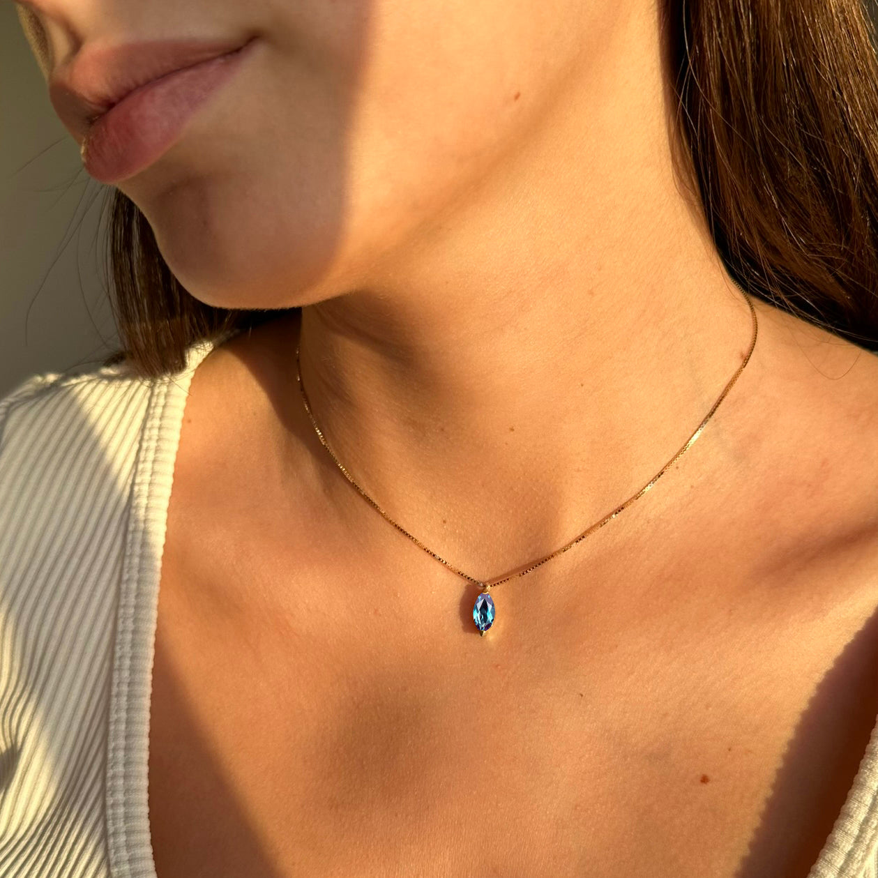 Close-up of a woman wearing a delicate necklace with a blue Alexandrite pendant.