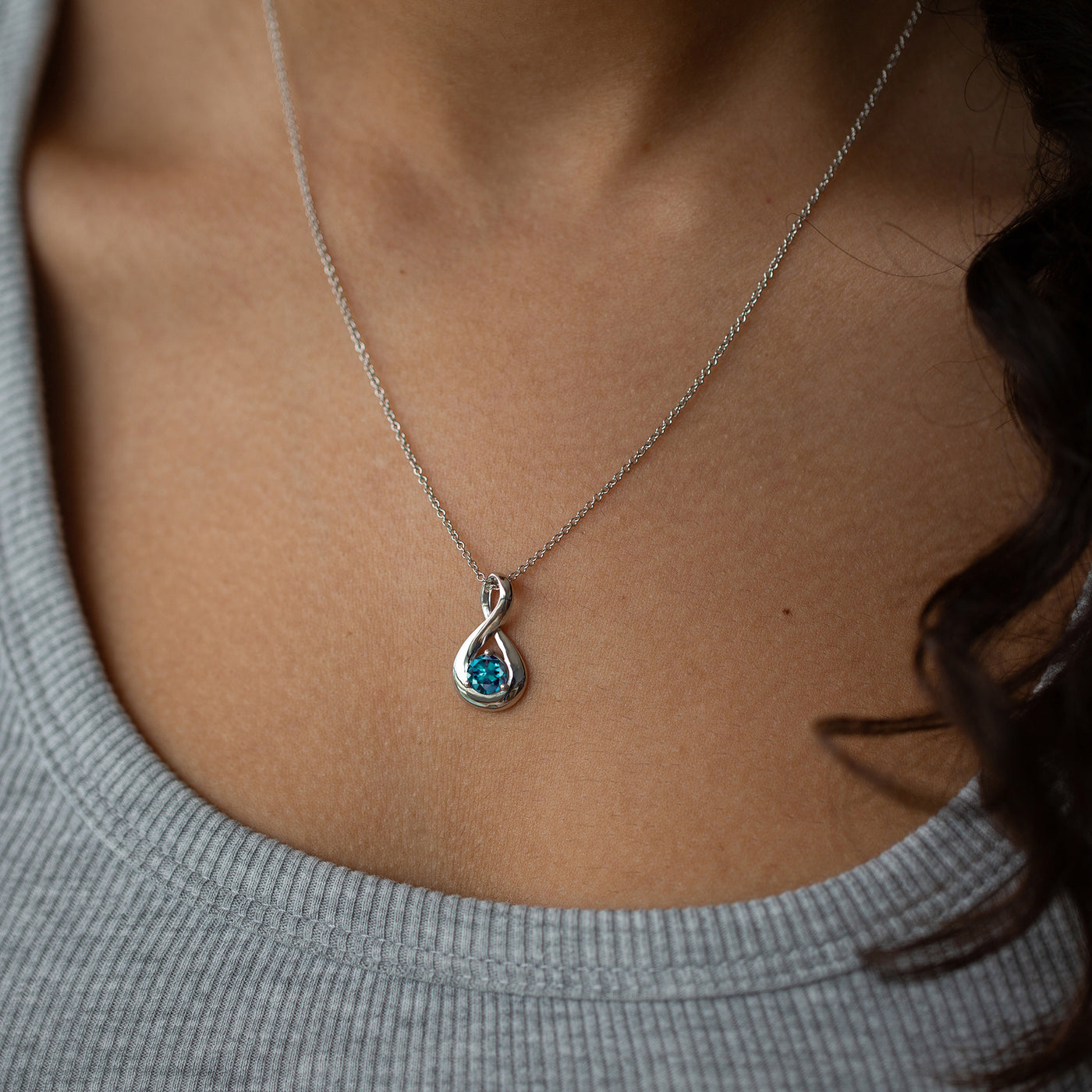 Necklace with a blue gemstone pendant worn by a person in a gray sweater.