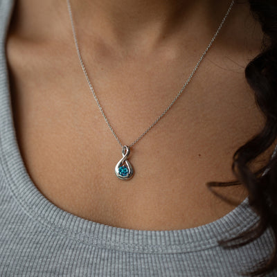 Necklace with a blue gemstone pendant worn by a person in a gray sweater.
