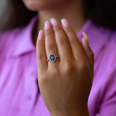 Hand wearing an alexandrite wedding ring against a blurred pink shirt background