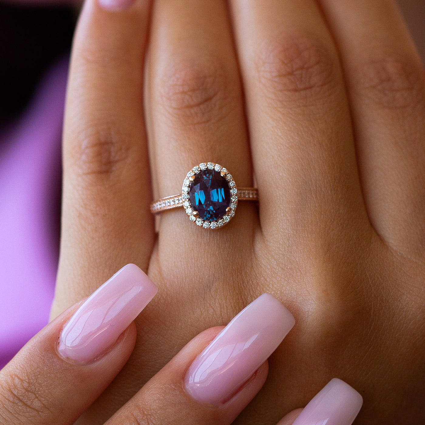 Close-up of a hand wearing an alexandrite engagement ring on a blurred background