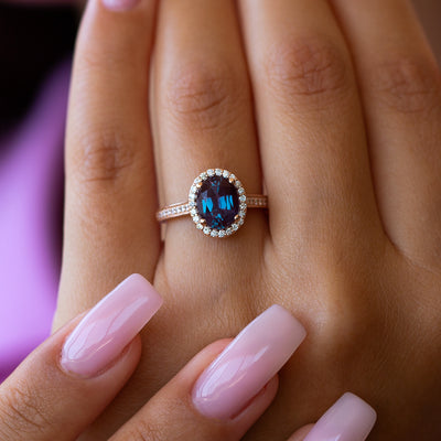 Close-up of a hand wearing an alexandrite engagement ring on a blurred background