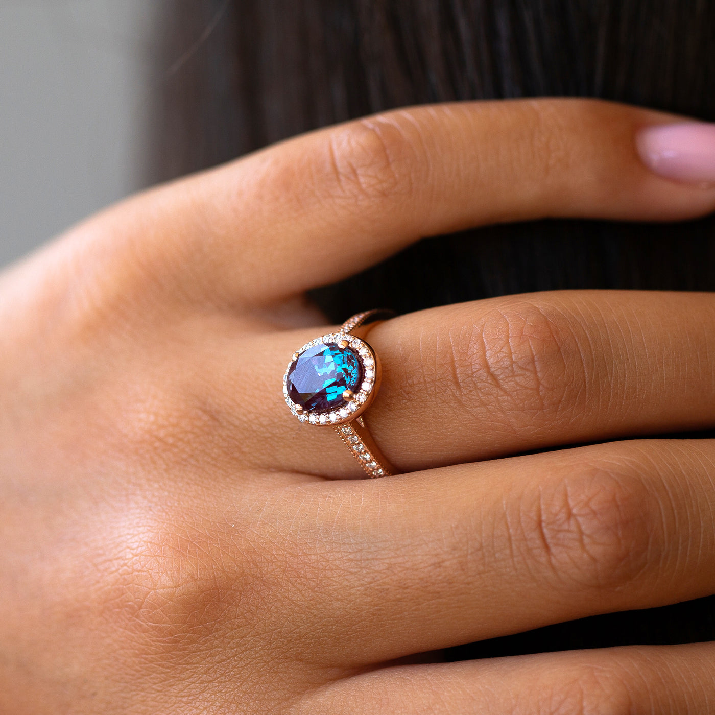 Close-up of a hand wearing a ring with a blue gemstone on a neutral background