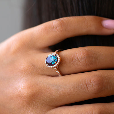 Close-up of a hand wearing a ring with a blue gemstone on a neutral background