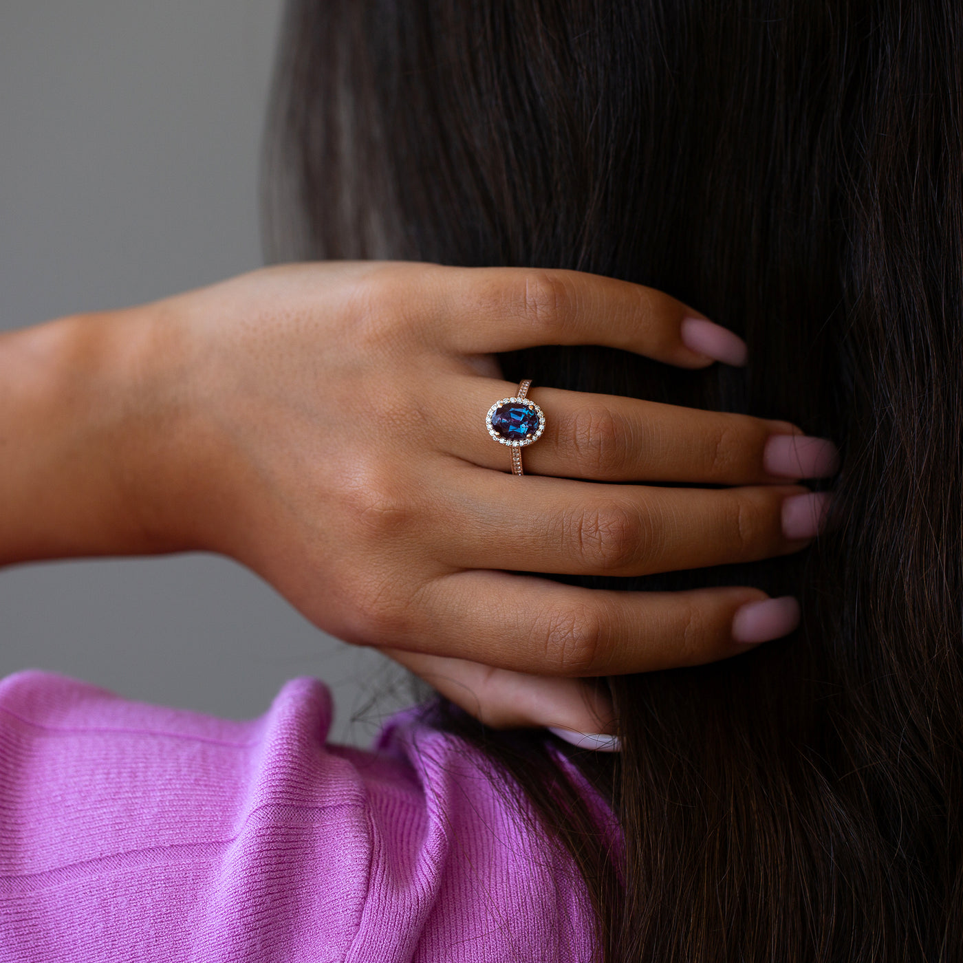 Close-up of a hand wearing an alexandrite and diamond ring with a blurred background