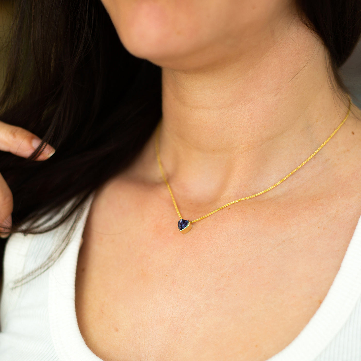 Close-up of a woman wearing a gold necklace with a blue heart pendant.