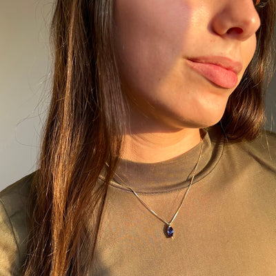 Close-up of a woman wearing a necklace with a blue alexandrite pendant.