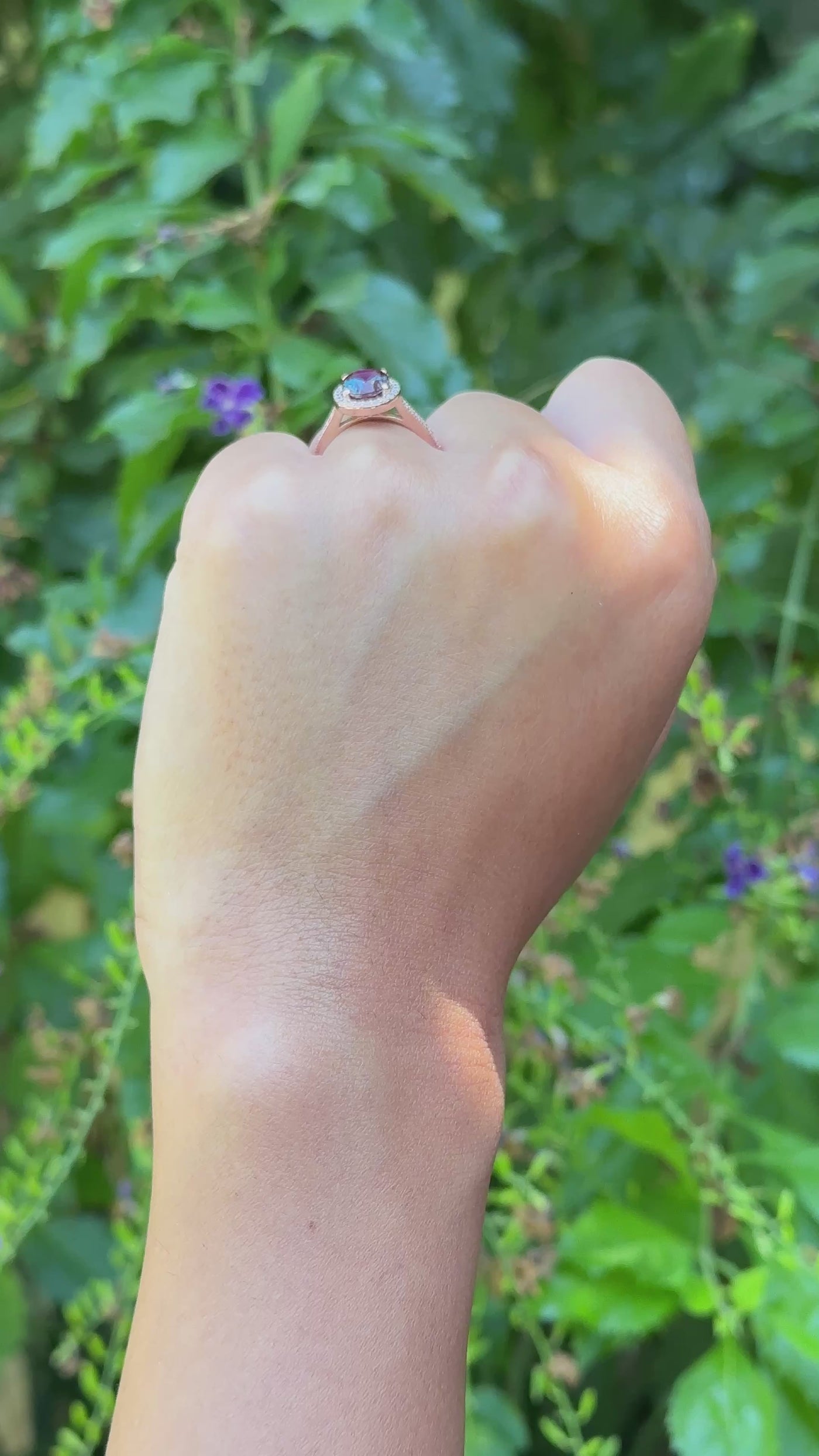 closeup of a and wearing a rose gold Alexandrite wedding ring with a diamond halo on a natural background