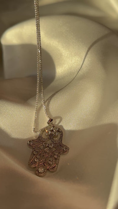 Gold hamsa necklace with diamonds on a white fabric background