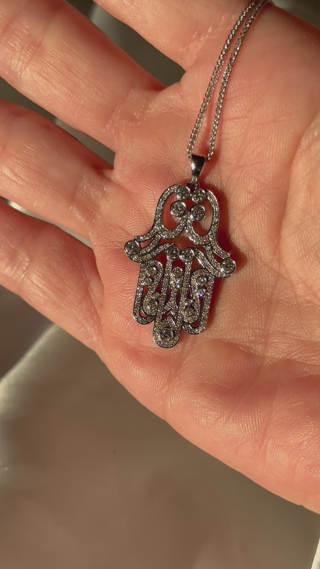 Hand holding a Hamsa pendant necklace with diamonds in 14K white gold