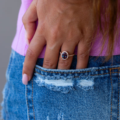 Close-up of a hand wearing a ring with a purple gemstone, holding blue jeans.