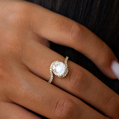 Twisted moissanite engagement ring with side diamonds on a person's finger against a dark background