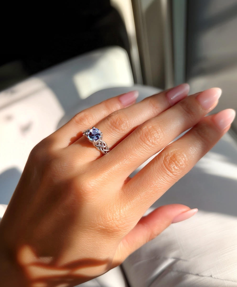 Hand wearing a Celtic engagement ring with a blue gemstone against a blurred background