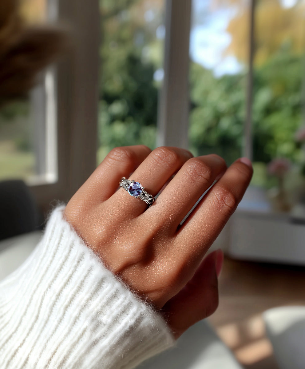 Hand wearing a celtic ring with a purple gemstone in front of a blurred indoor background