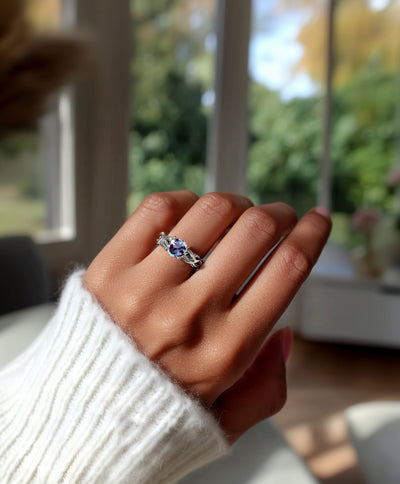 Hand wearing a celtic ring with a purple gemstone in front of a blurred indoor background