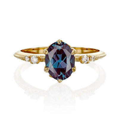 Gold engagement ring with a purple gemstone and small diamonds on a white background